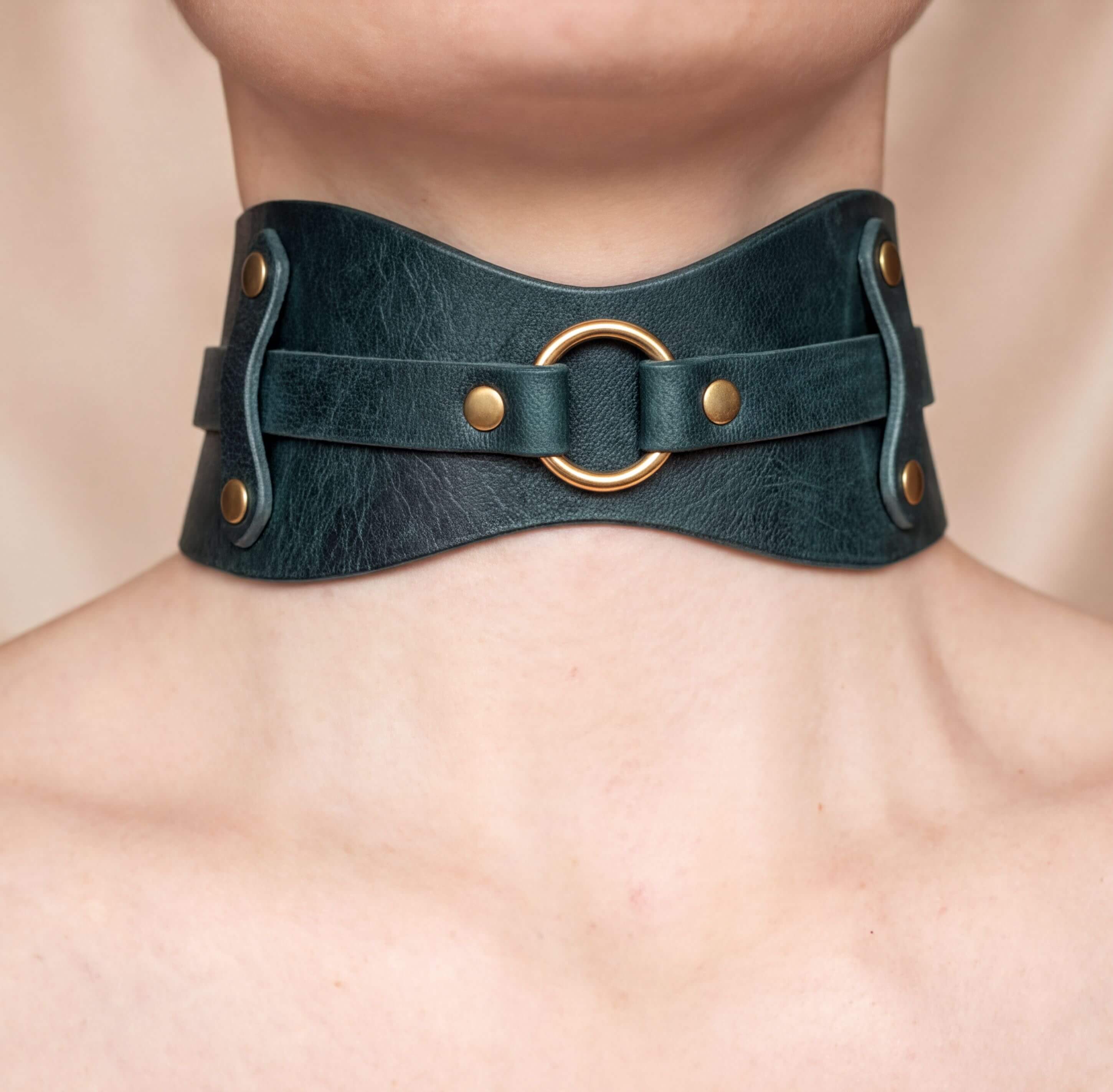 A close-up view of a person's neck and chest area wearing a dark green leather choker necklace with a gold ring.