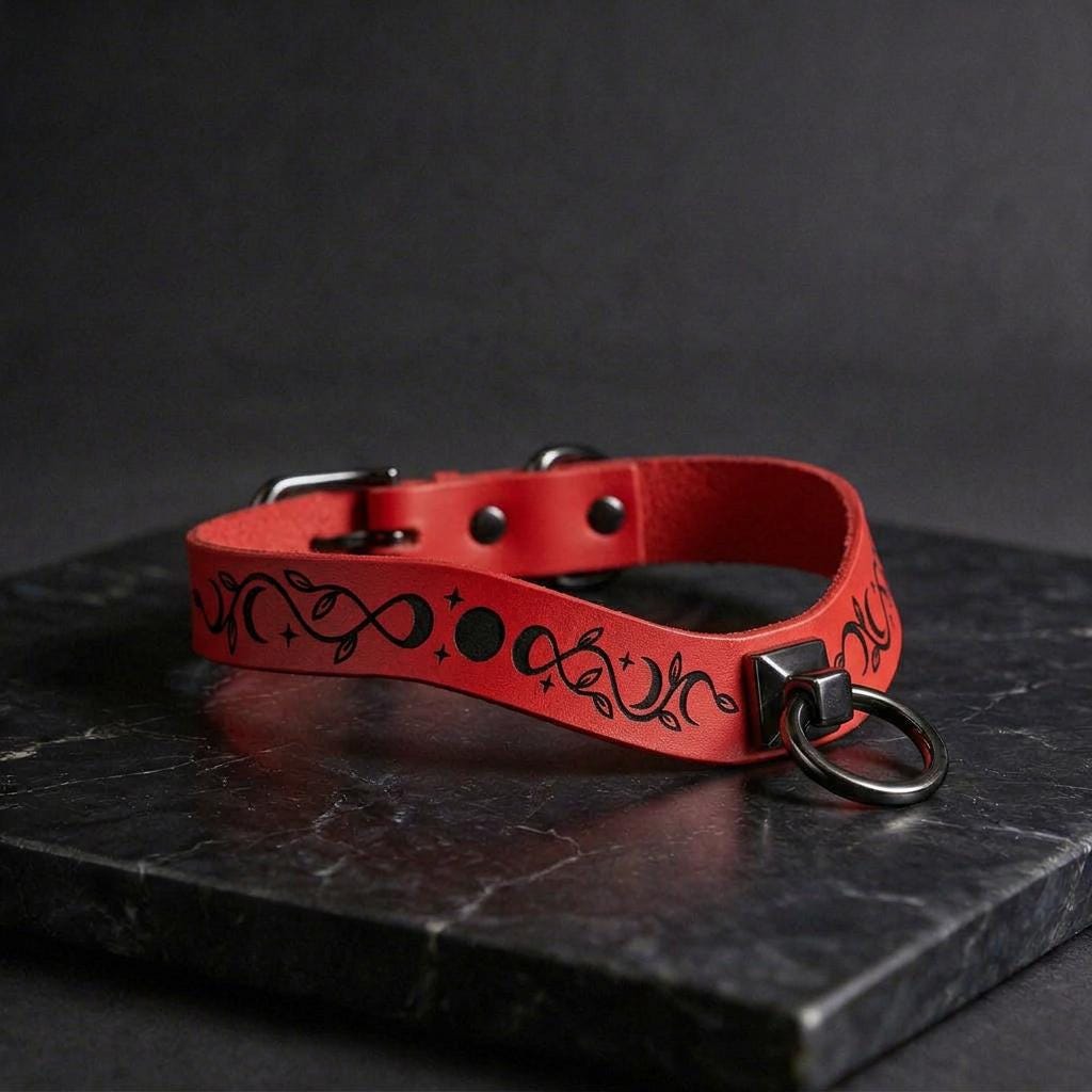 A red leather choker necklace with a black floral design on the band and a black metal ring on the front.