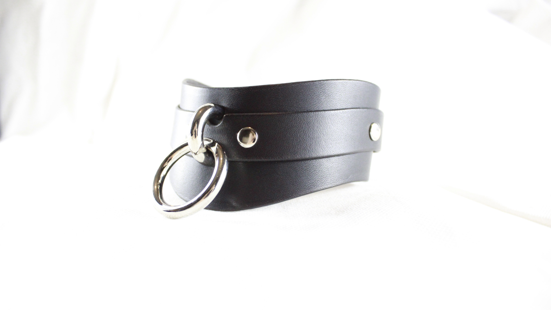A black leather choker necklace with a silver ring and two holes on the front.