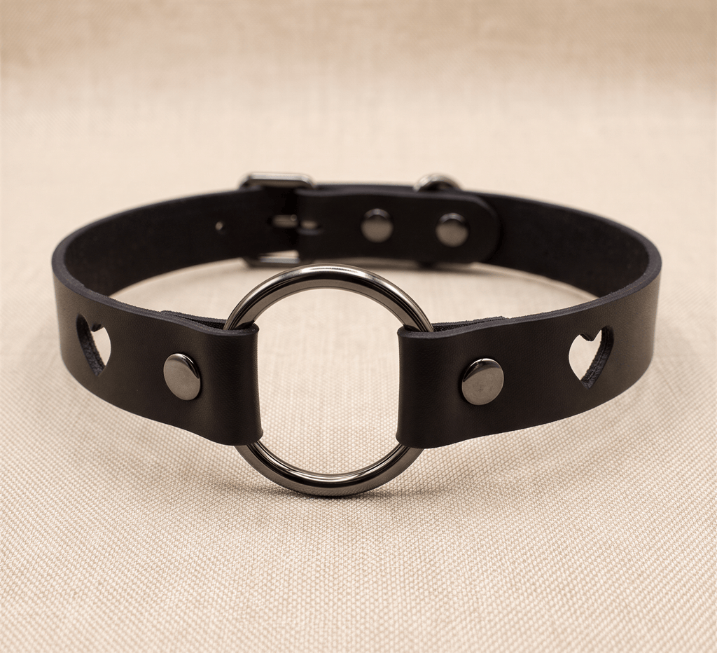 A black leather choker collar with a round metal ring and heart-shaped cutouts on either side.