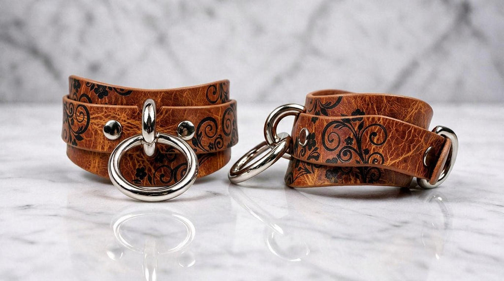 Two brown leather straps with metal rings and buckles are displayed on a marble surface.