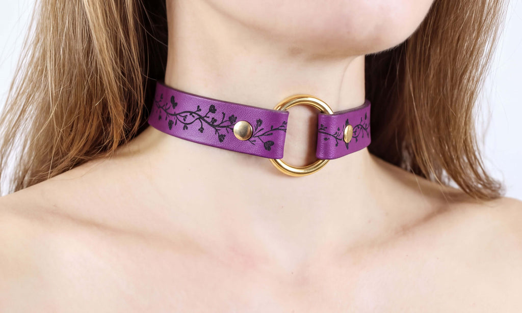 A close-up of a person's neck wearing a purple choker necklace with a gold ring.