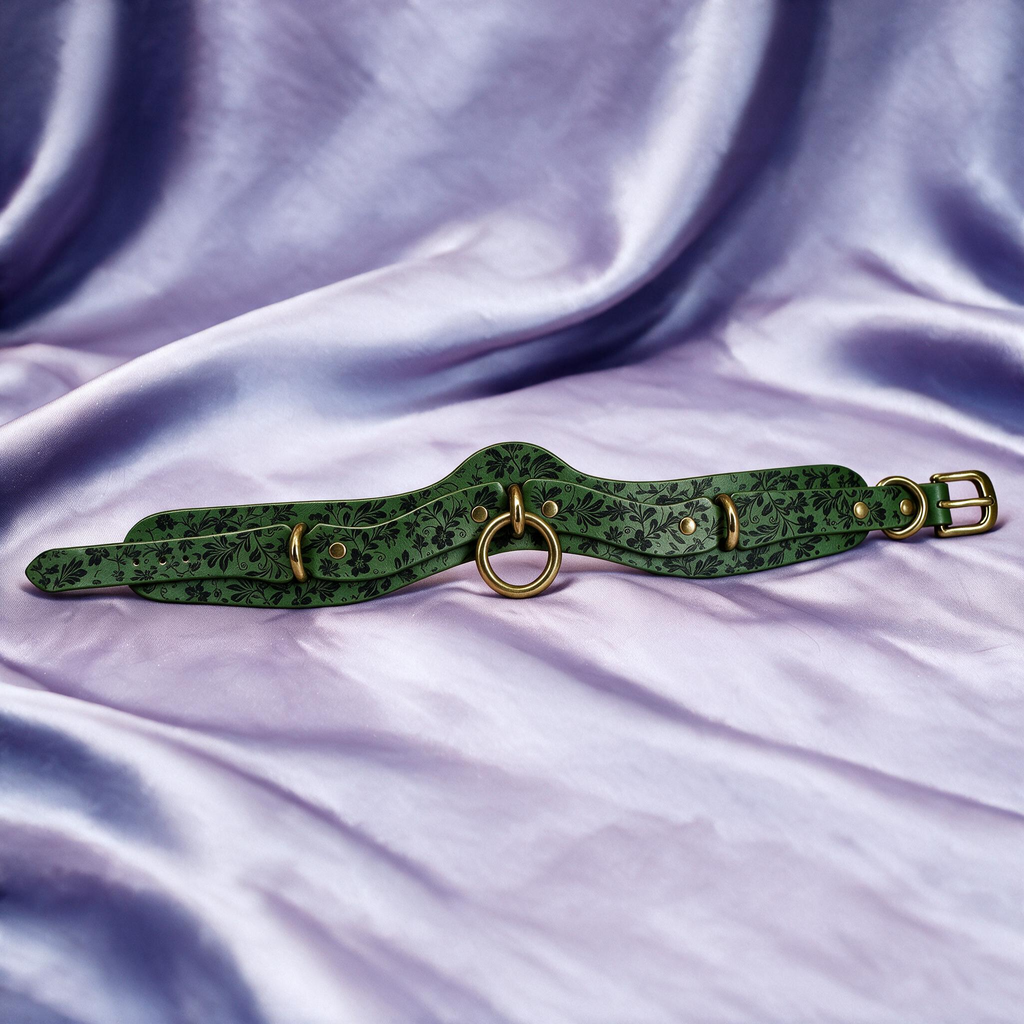 A green leather choker necklace with metal rings and buckles is displayed on a purple fabric background.