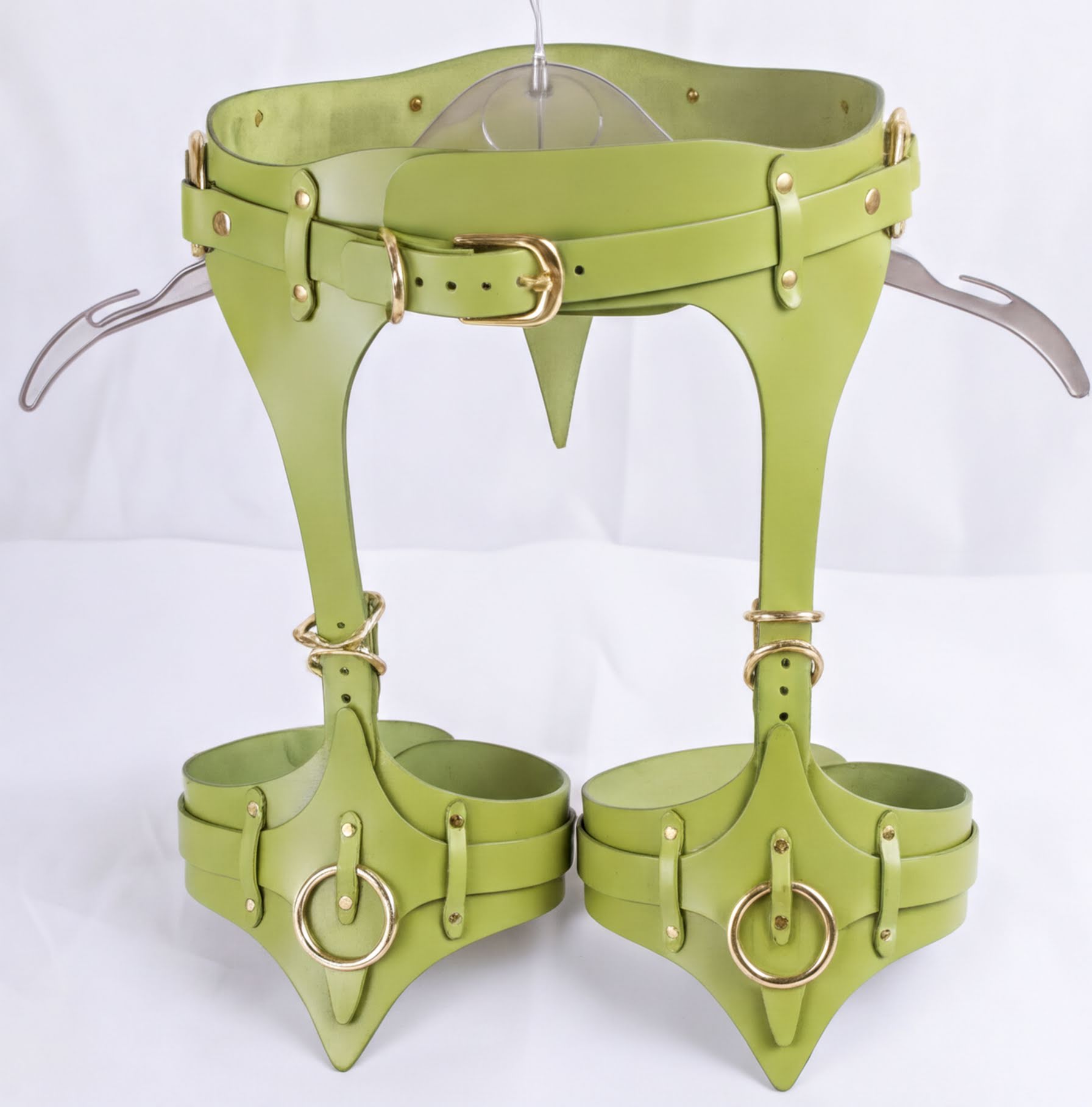 A pair of green leather corsets with metal rings and straps, designed for corsetry or body shaping purposes.