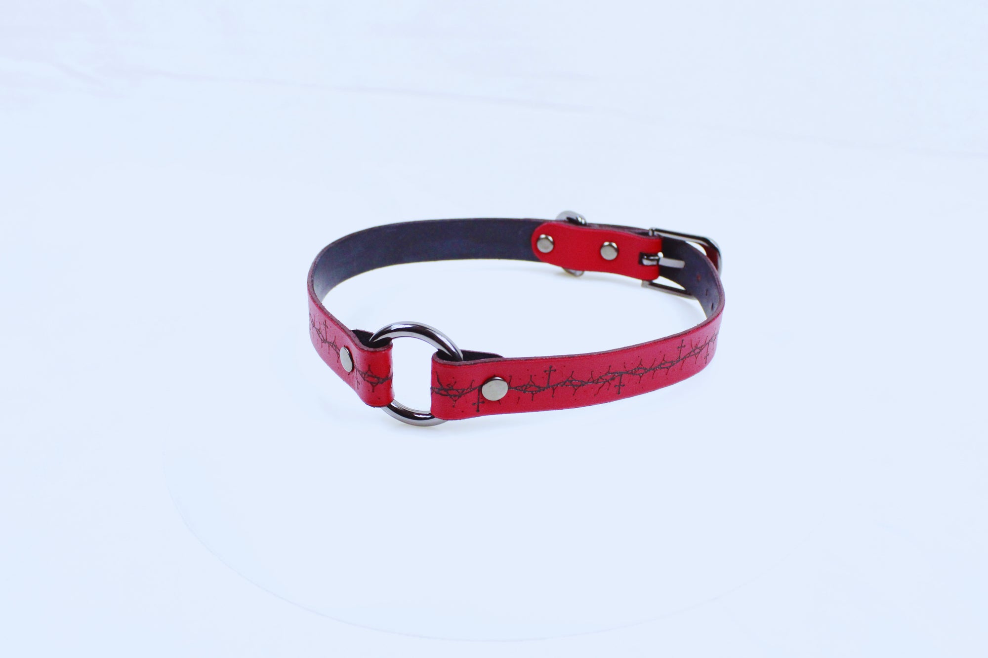 A red leather collar with metal rings and a decorative pattern on the strap.