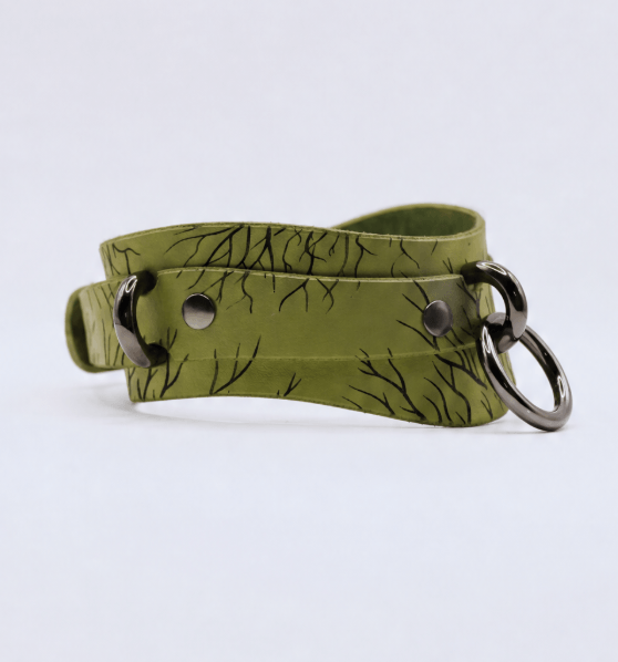 A green leather choker necklace with a black tree branch pattern and metal rings.