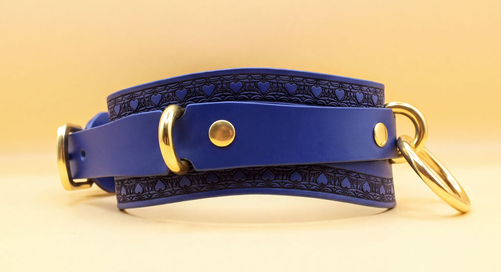 A blue leather choker collar with gold hardware, including a buckle and two rings, is shown against a yellow background.