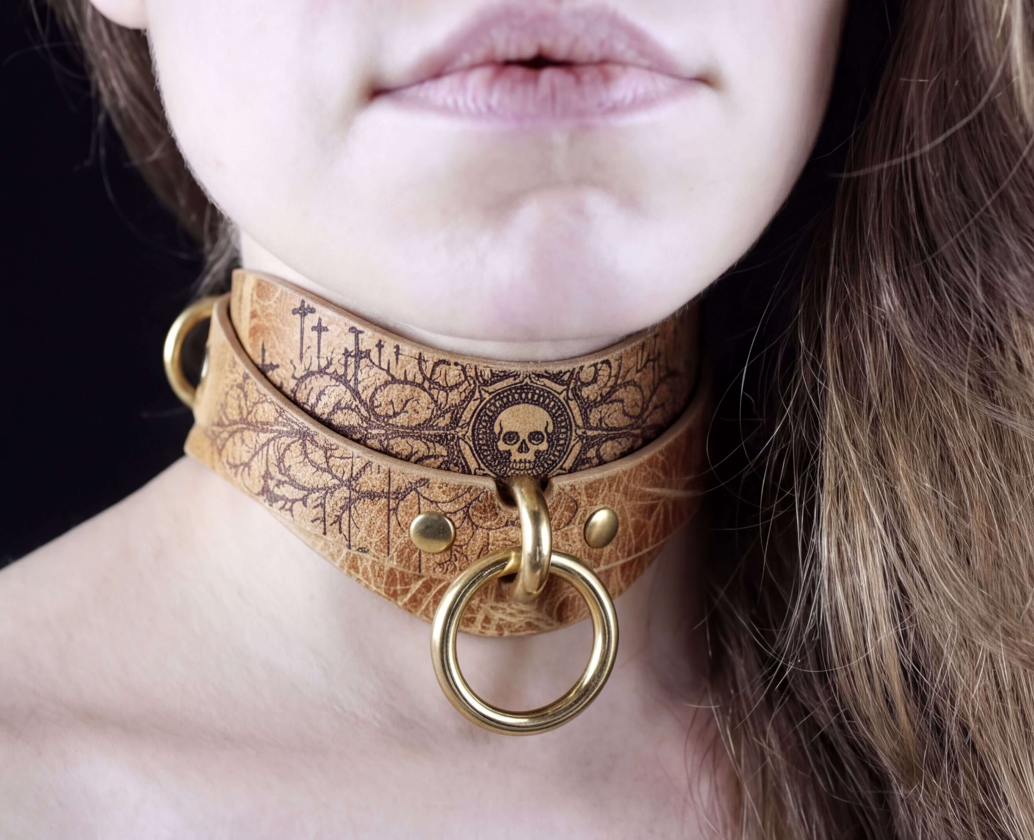 A close-up of a woman's neck and chin wearing a leather choker necklace with a skull design and a gold ring.