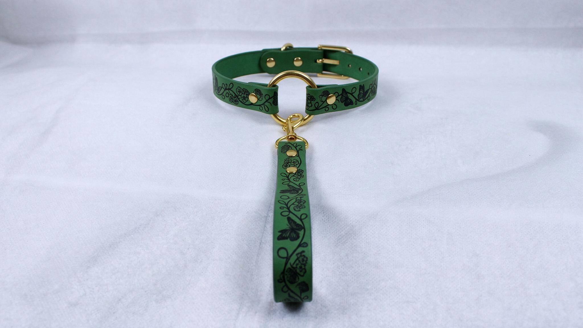 A green collar with a gold buckle and a green leash attached to it, resting on a white surface.