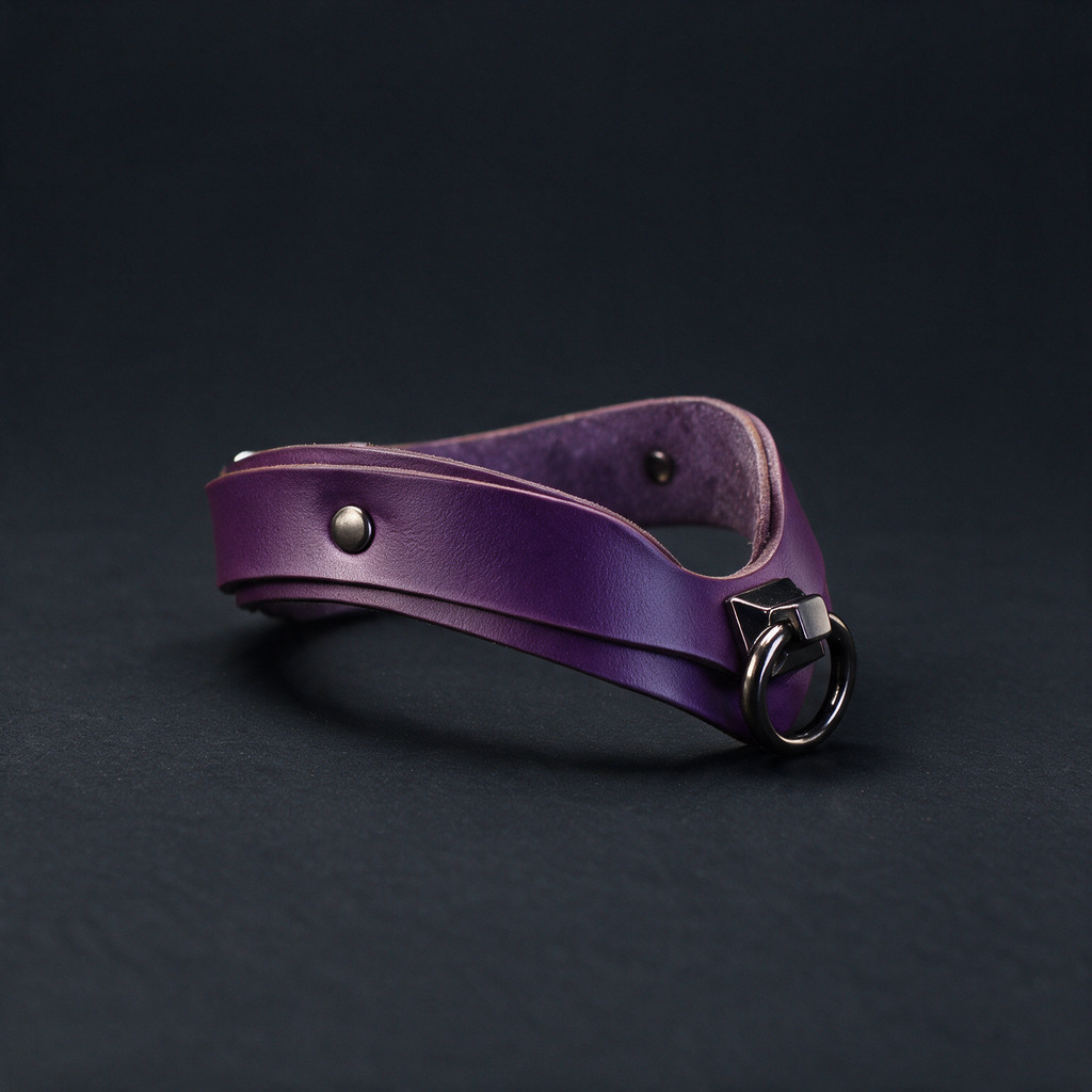 A purple leather choker necklace with a metal clasp and a small metal button on the front is shown against a dark background.