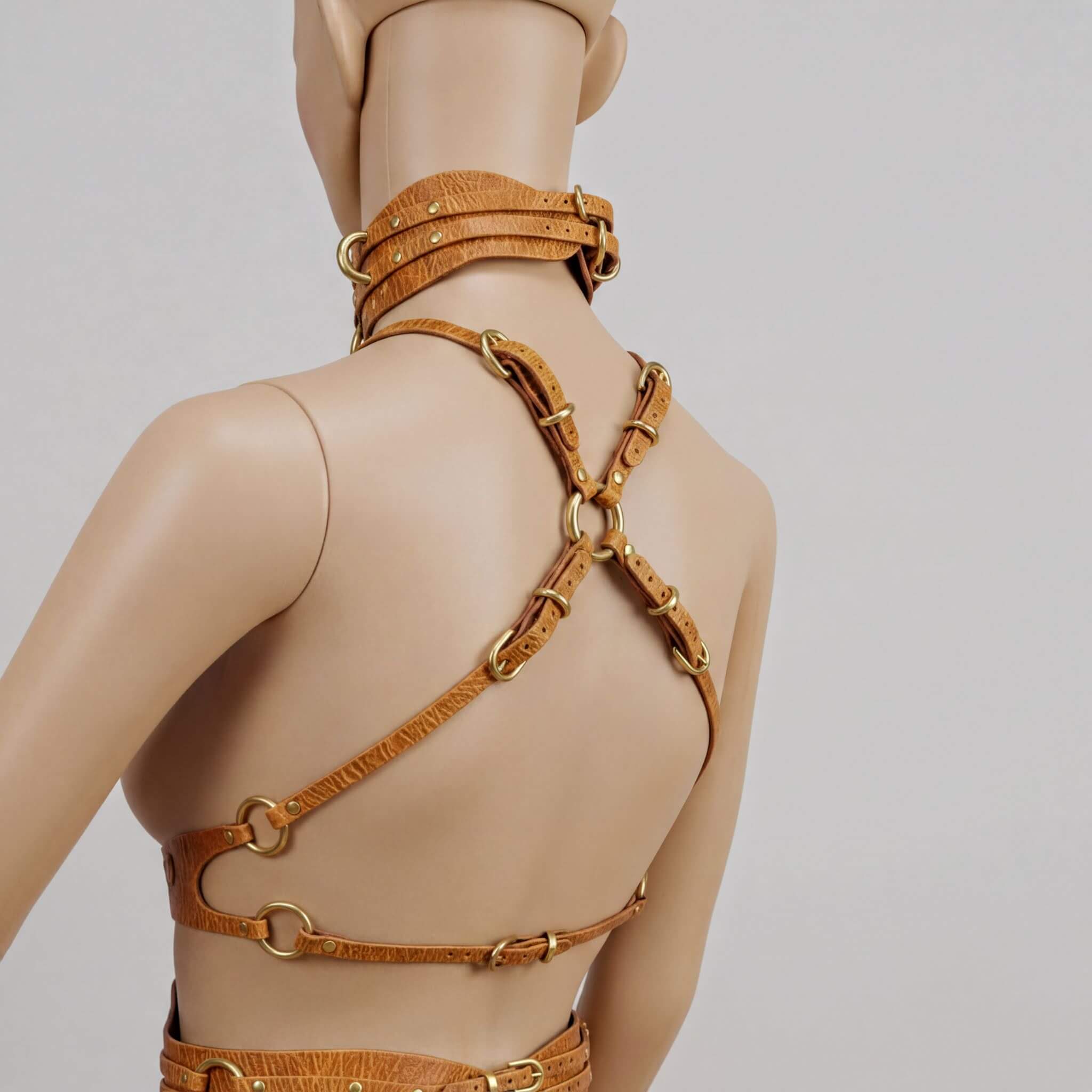 A mannequin wearing a leather strap with gold rings and buckles, creating a unique and eye-catching design.