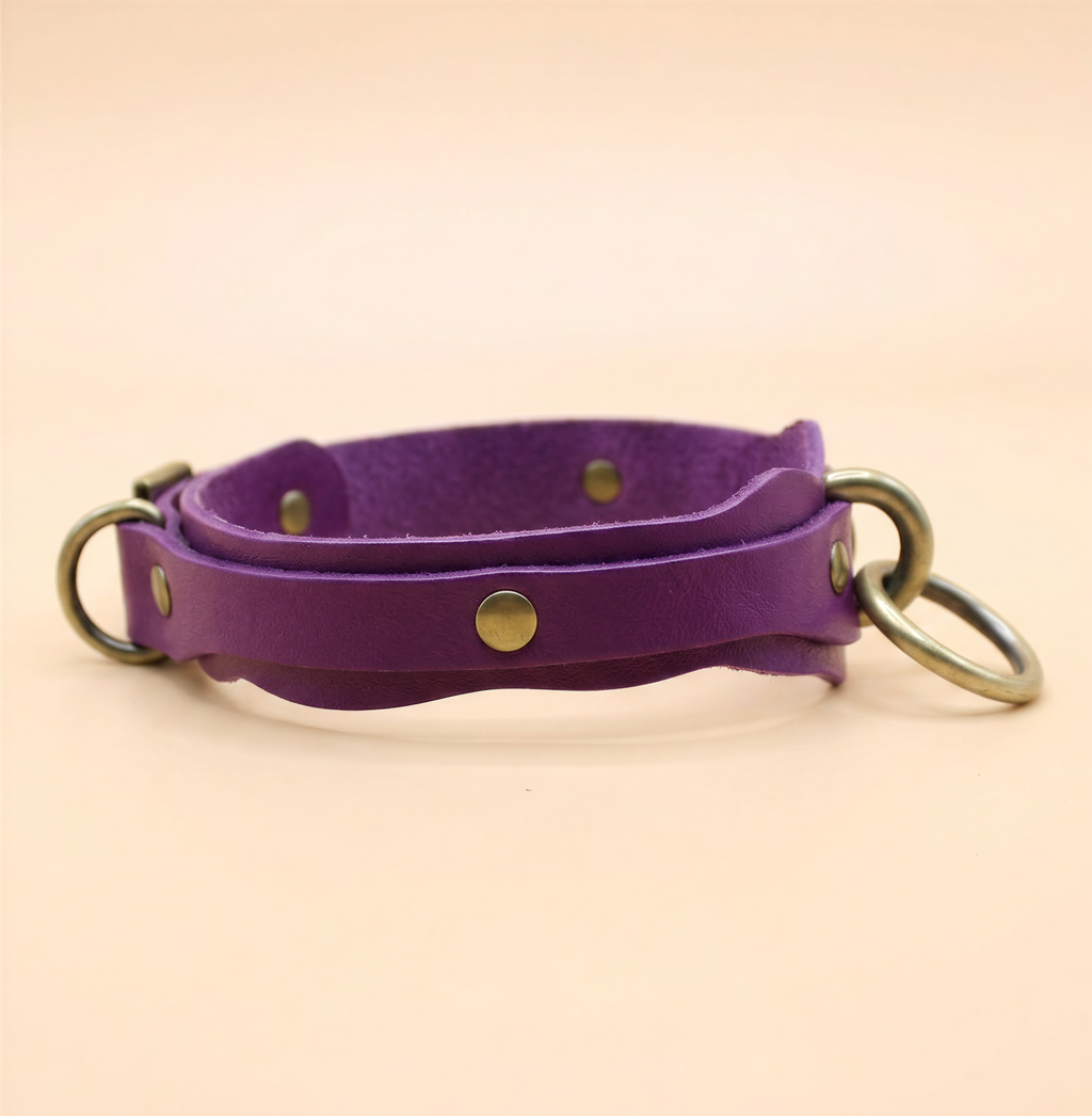 A purple leather collar with metal rings and buckles.
