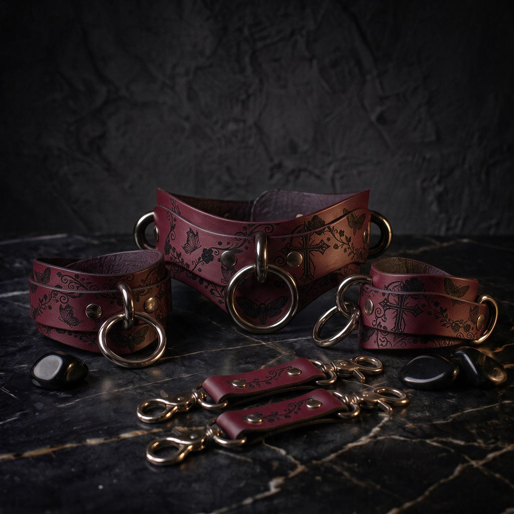 A set of burgundy leather choker necklaces and straps with intricate floral designs, displayed on a dark surface.