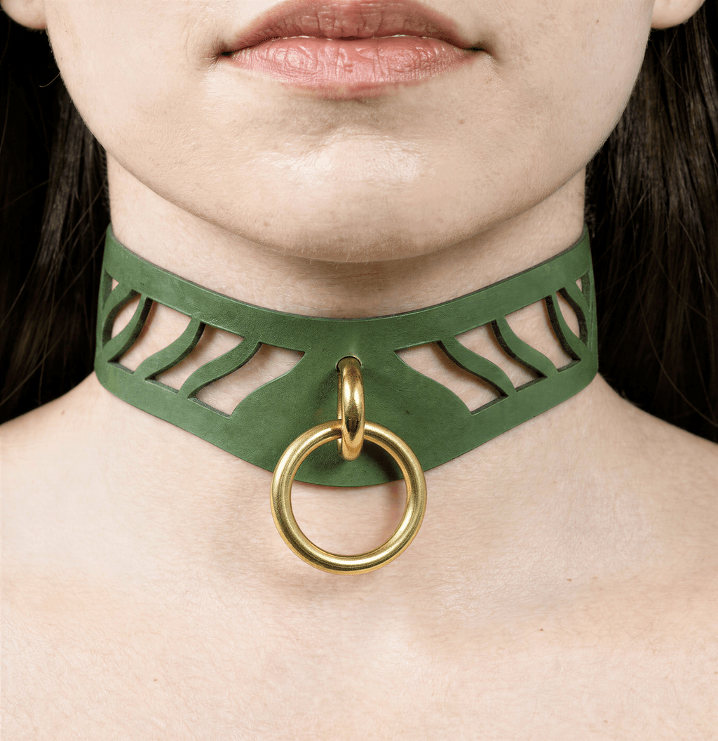 A close-up of a person's neck and chest area, featuring a green choker necklace with a gold ring and a cutout design.