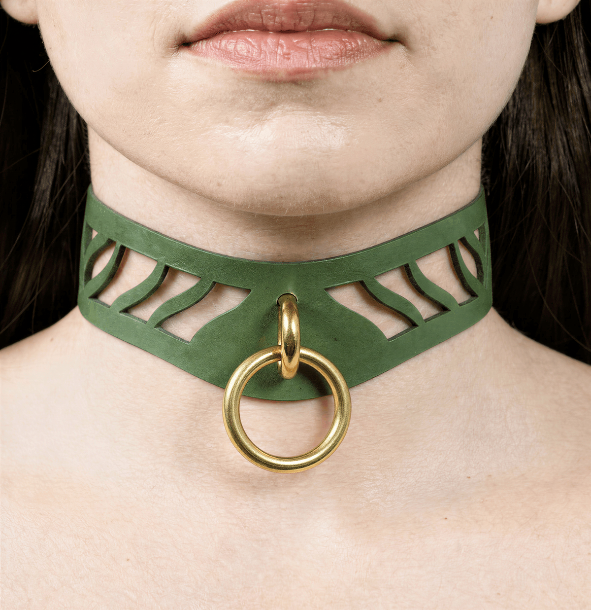 A close-up of a person's neck and chest area, featuring a green choker necklace with a gold ring and a cutout design.