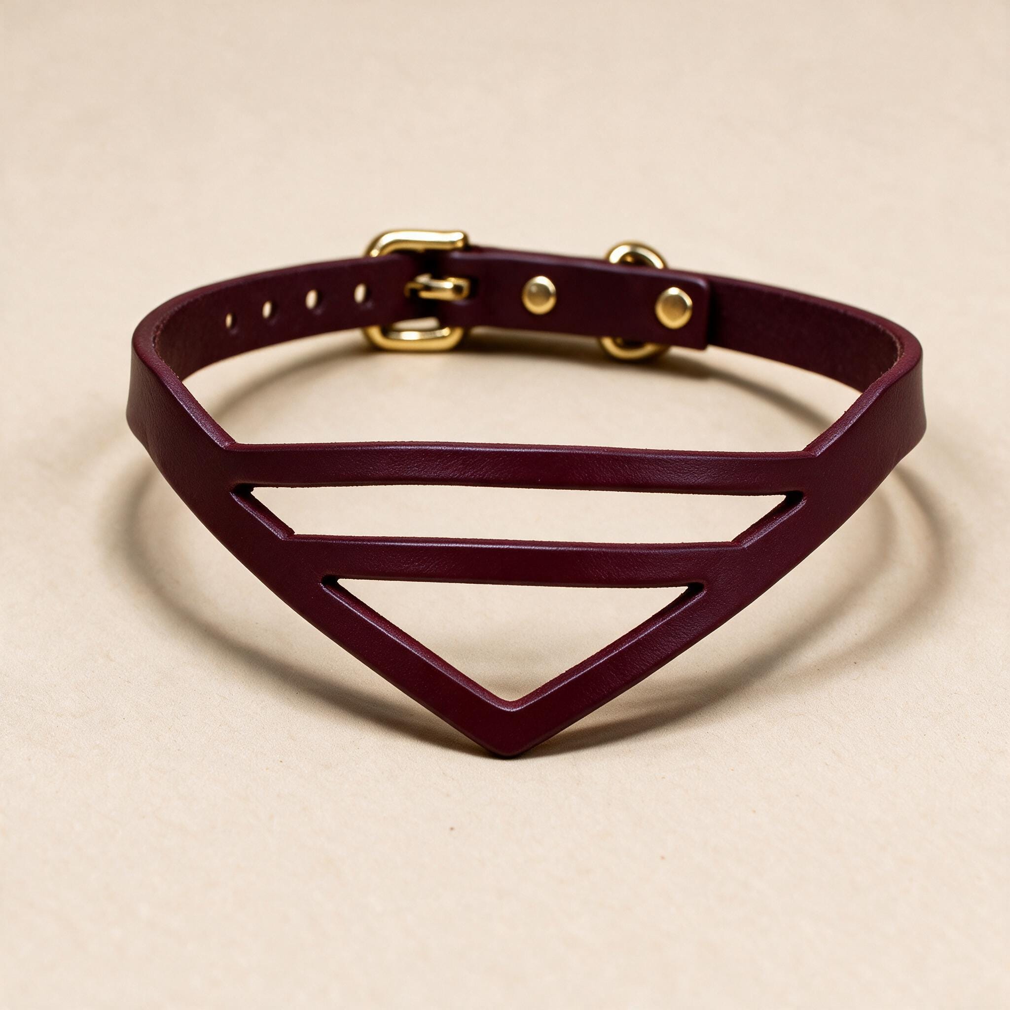A burgundy leather choker necklace with a geometric design and a gold buckle.