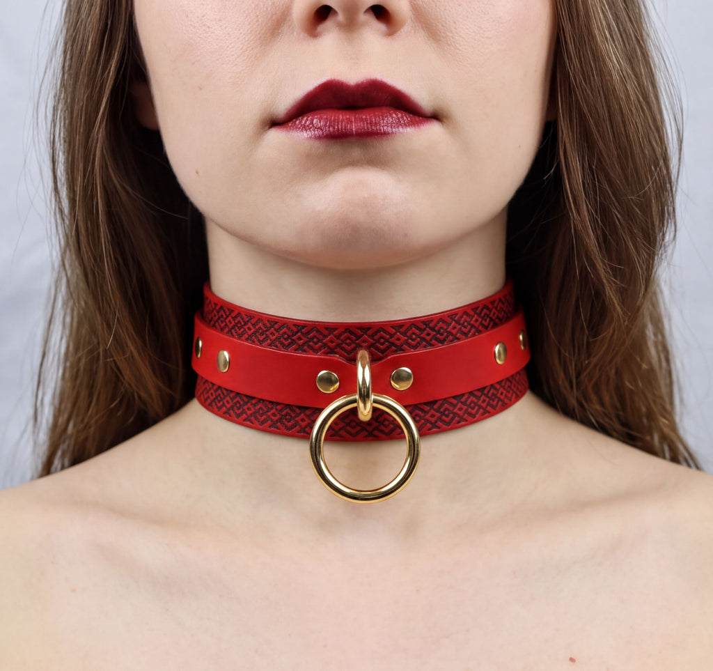 A close-up of a woman's neck and chest area wearing a red choker necklace with a gold ring.