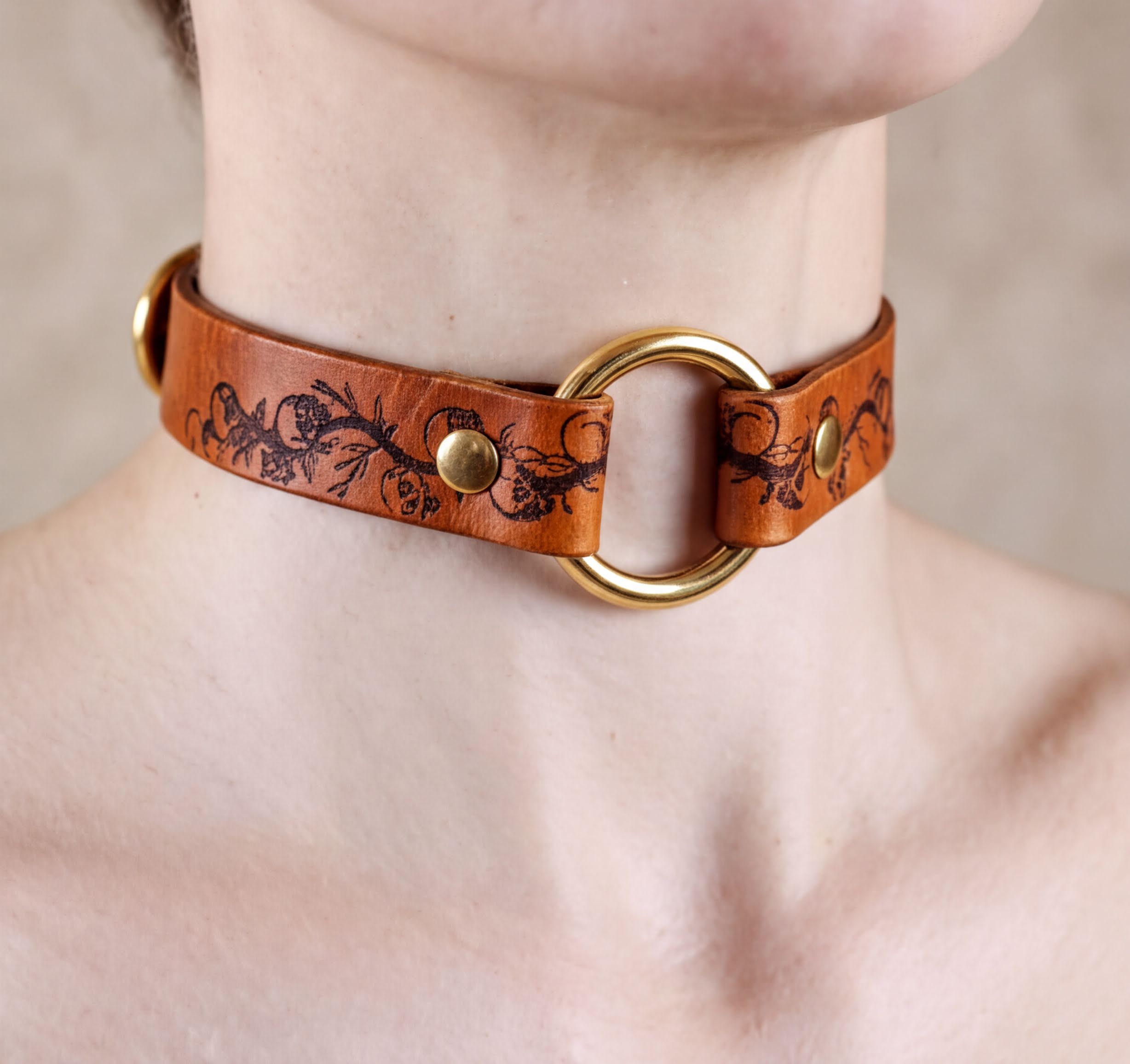 A close-up image of a person wearing a brown leather choker necklace with a gold ring and floral design.