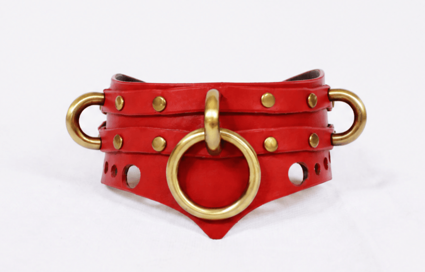 A red leather collar with gold metal rings and studs, featuring a distinctive design.