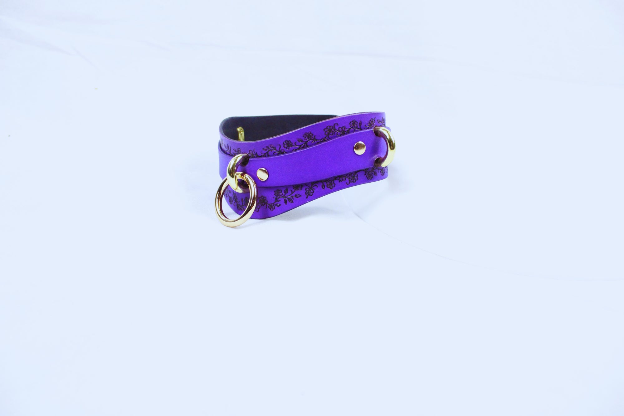 A purple leather choker necklace with a floral pattern and gold-colored metal rings.
