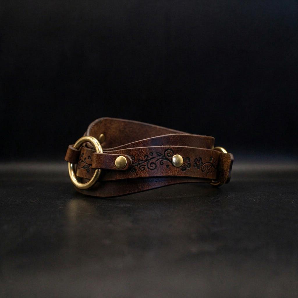 A brown leather belt with a decorative floral pattern and two gold-colored buckles is displayed against a black background.