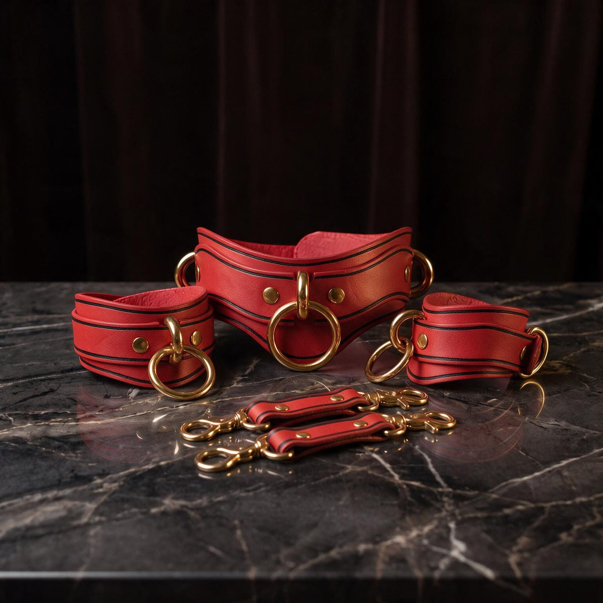 A set of red leather straps with gold hardware, including buckles and clasps, arranged on a marble surface.