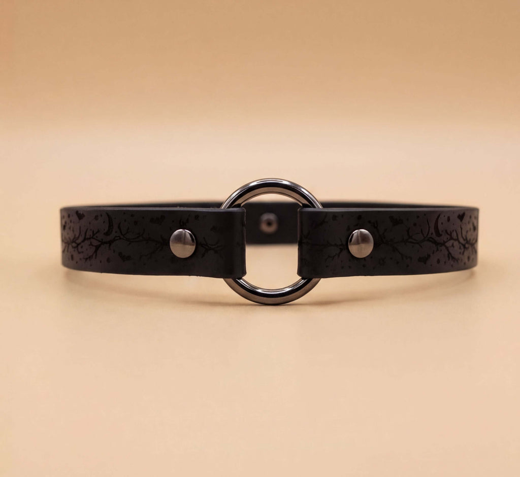 A black leather choker necklace with a circular metal ring and two metal buttons.