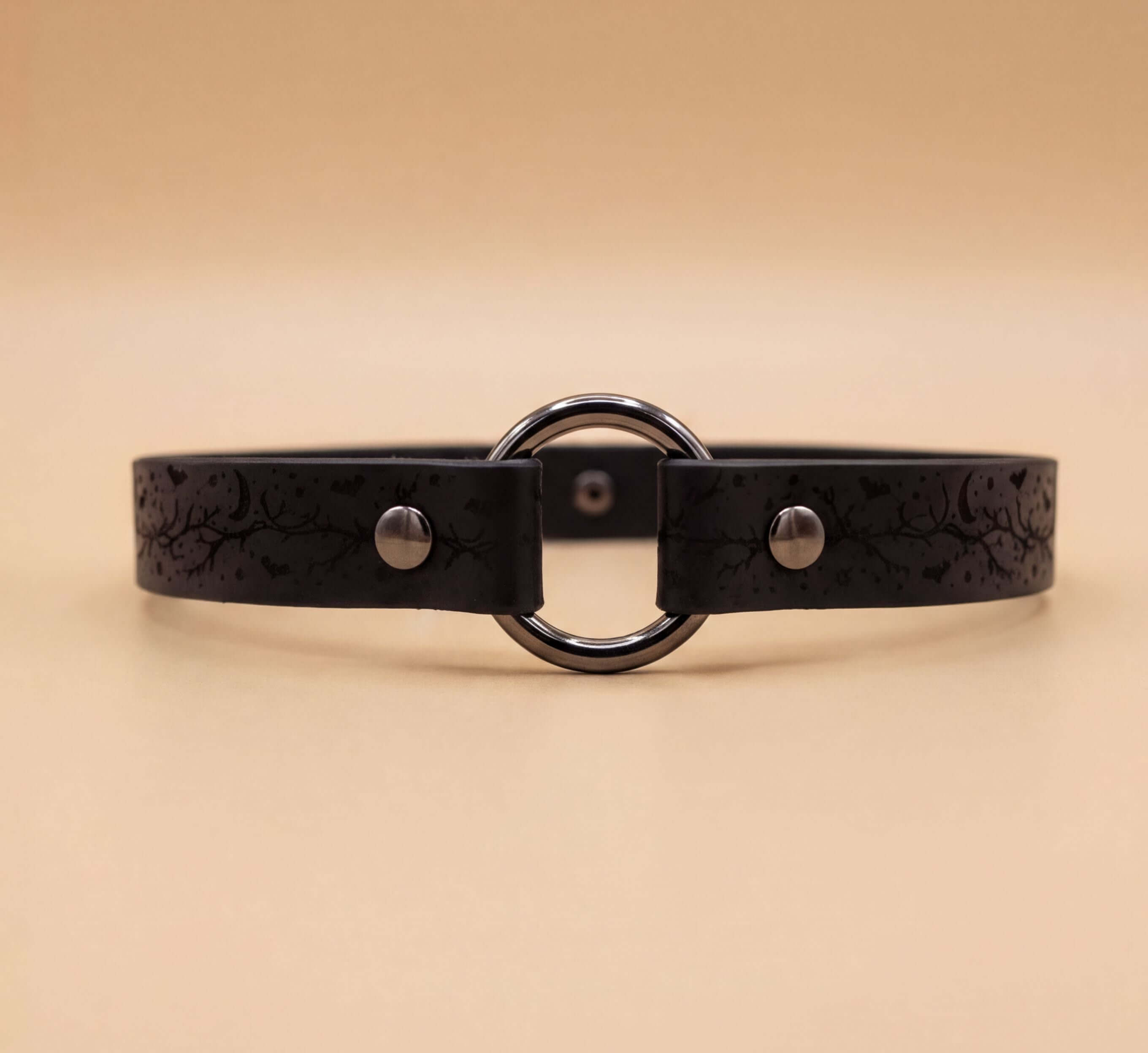 A black leather choker necklace with a circular metal ring and two metal buttons.