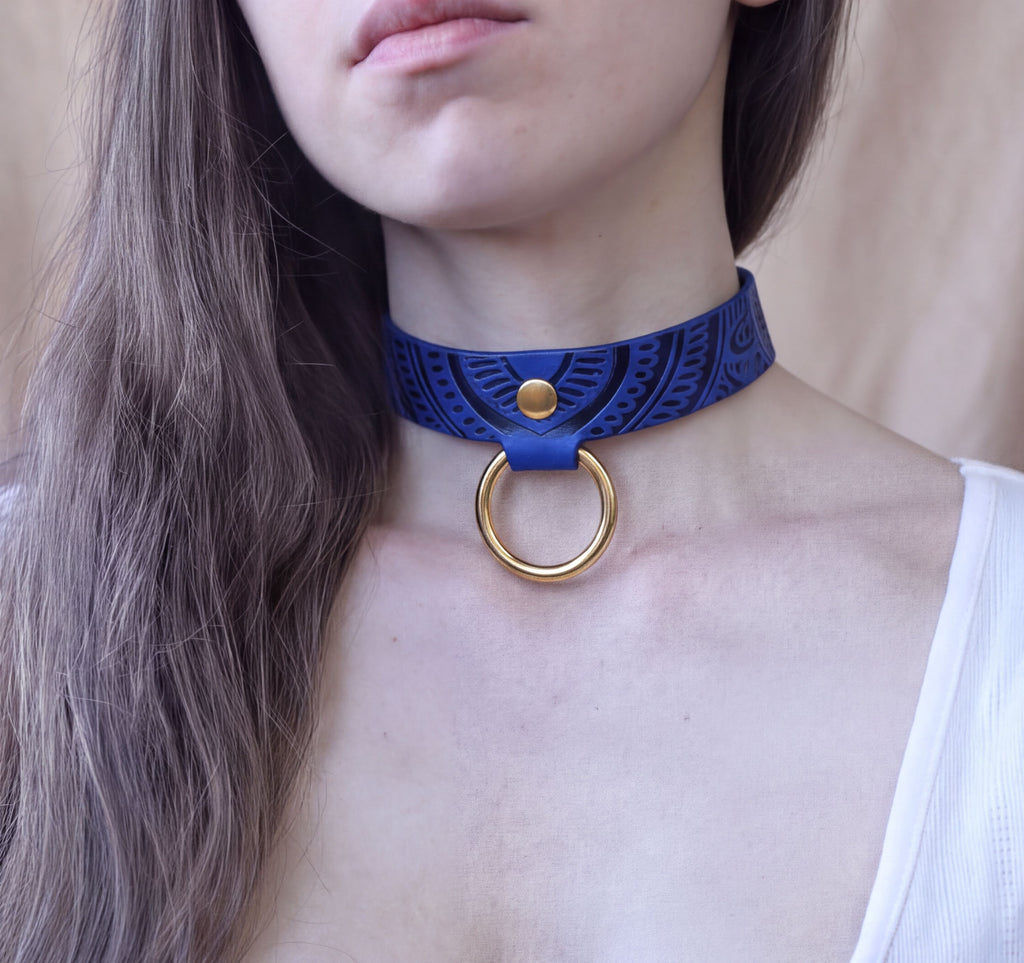 A close-up of a woman's neck and chest area wearing a blue choker necklace with a gold ring.