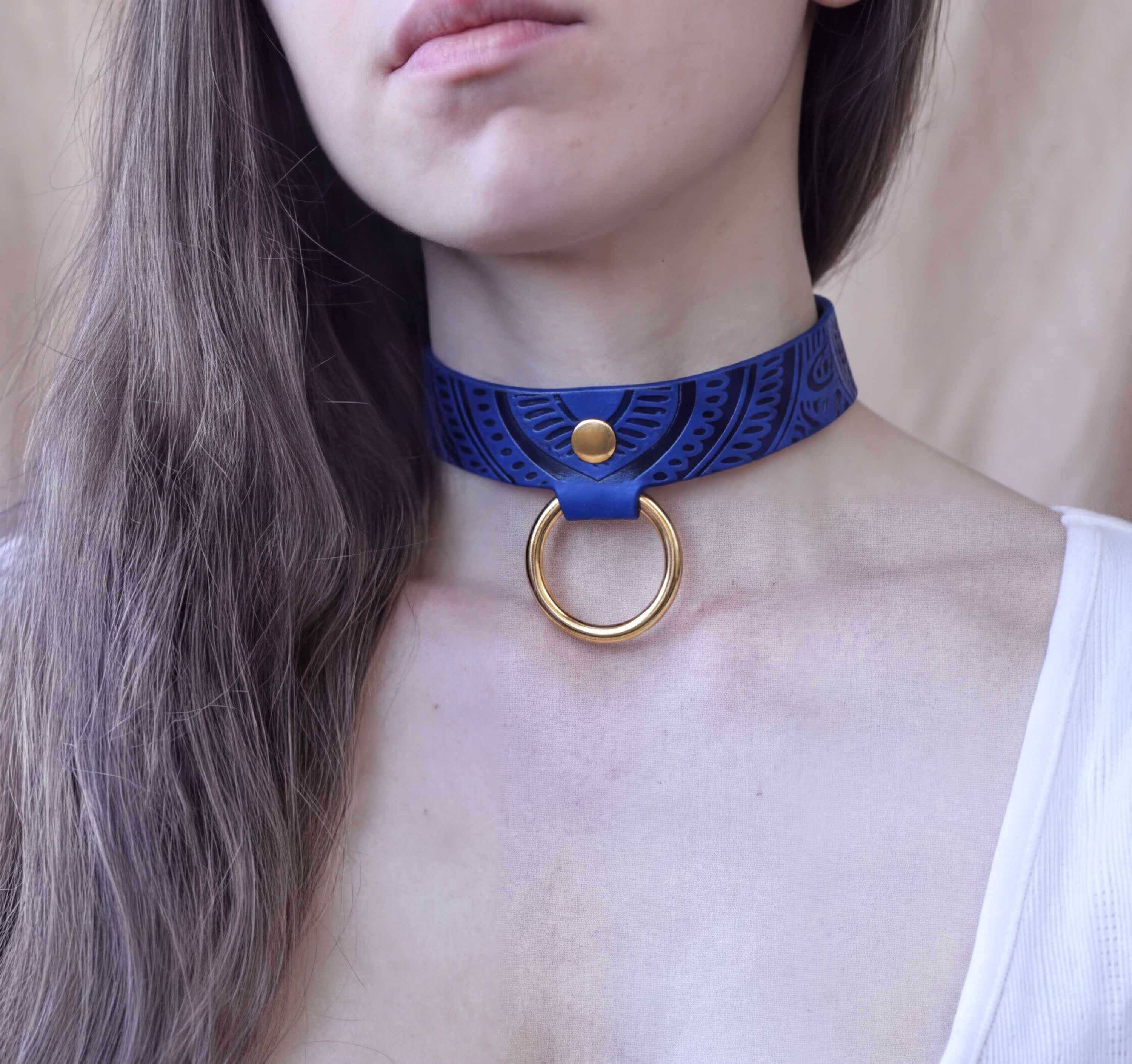 A close-up of a woman's neck and chest area wearing a blue choker necklace with a gold ring.