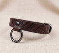 A brown leather collar with a metal ring and buckle, placed on a beige fabric background.