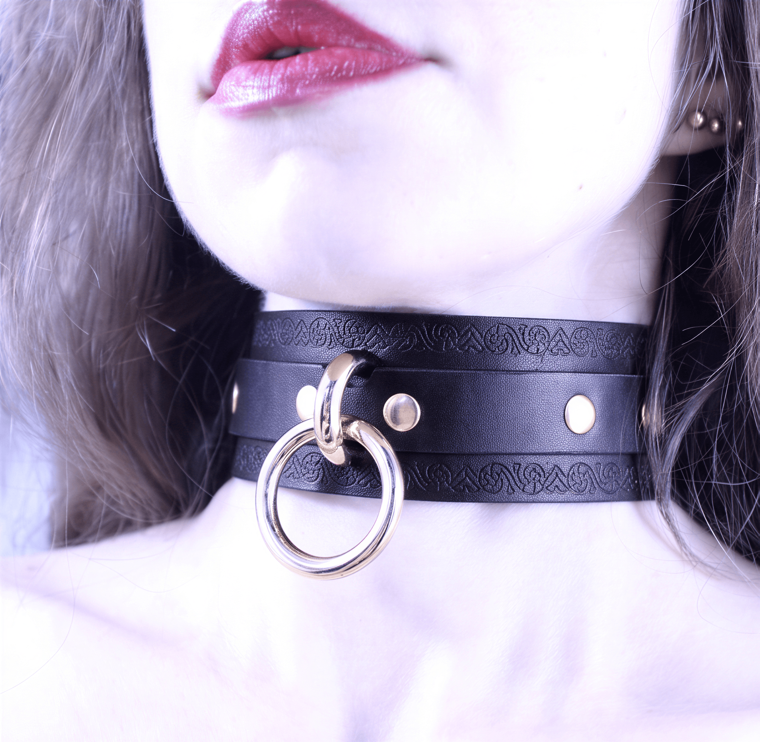 A close-up of a woman's face wearing a black choker necklace with a gold ring and buckle.