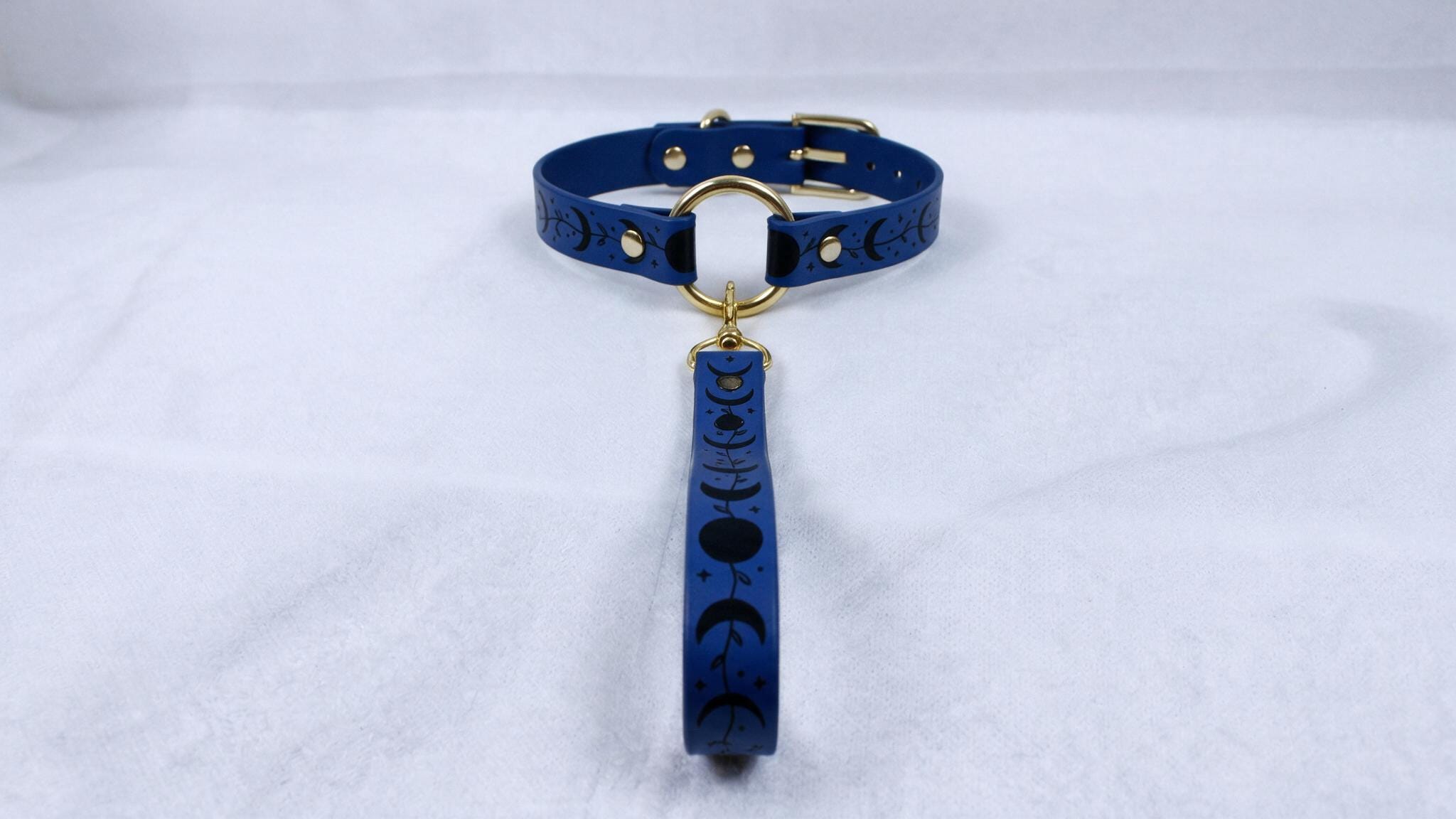 A blue collar with a moon and crescent design, featuring a gold buckle and a dangling handle.