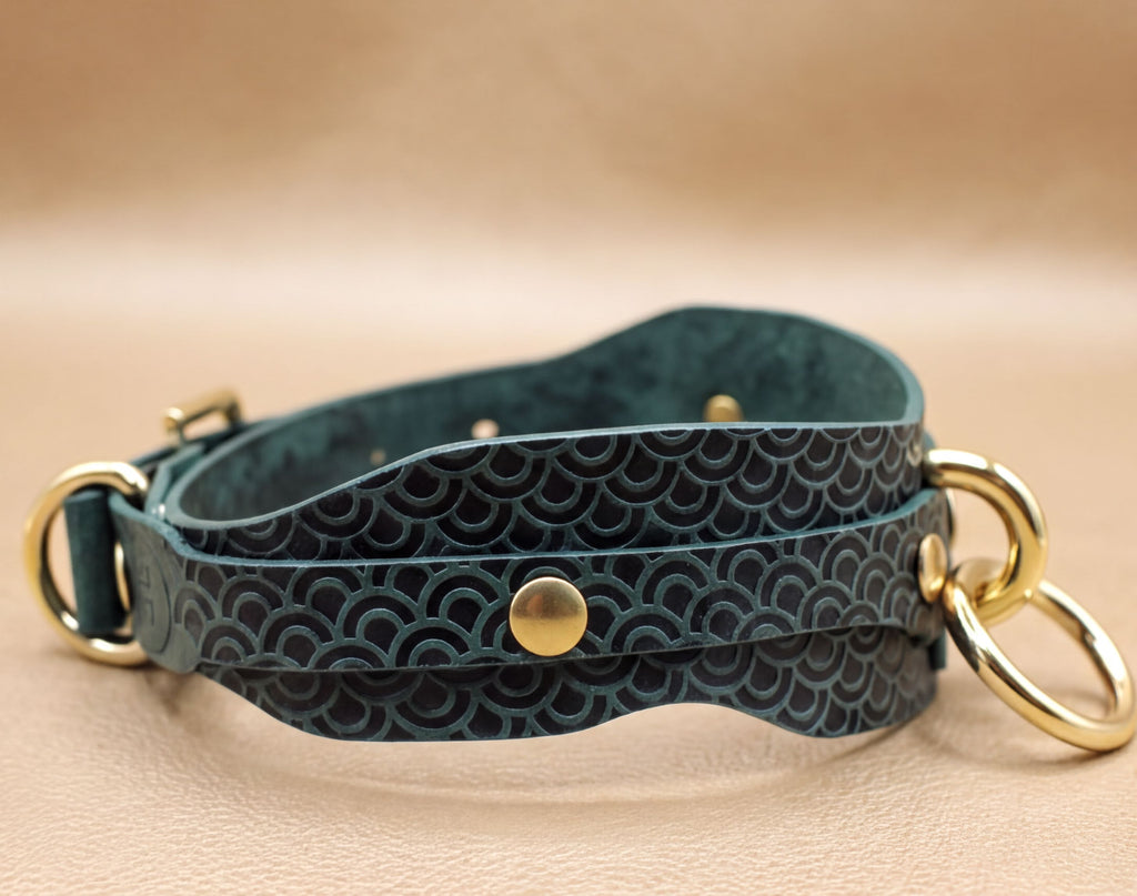 A dark green leather choker necklace with a patterned design and two gold-colored metal rings on either side.