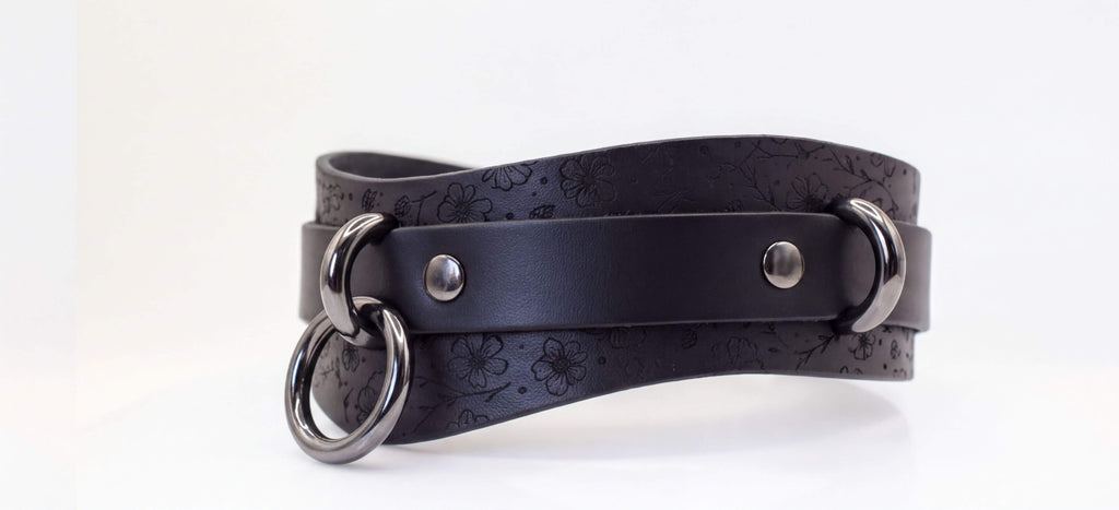 A black leather choker necklace with metal rings and a metal buckle.