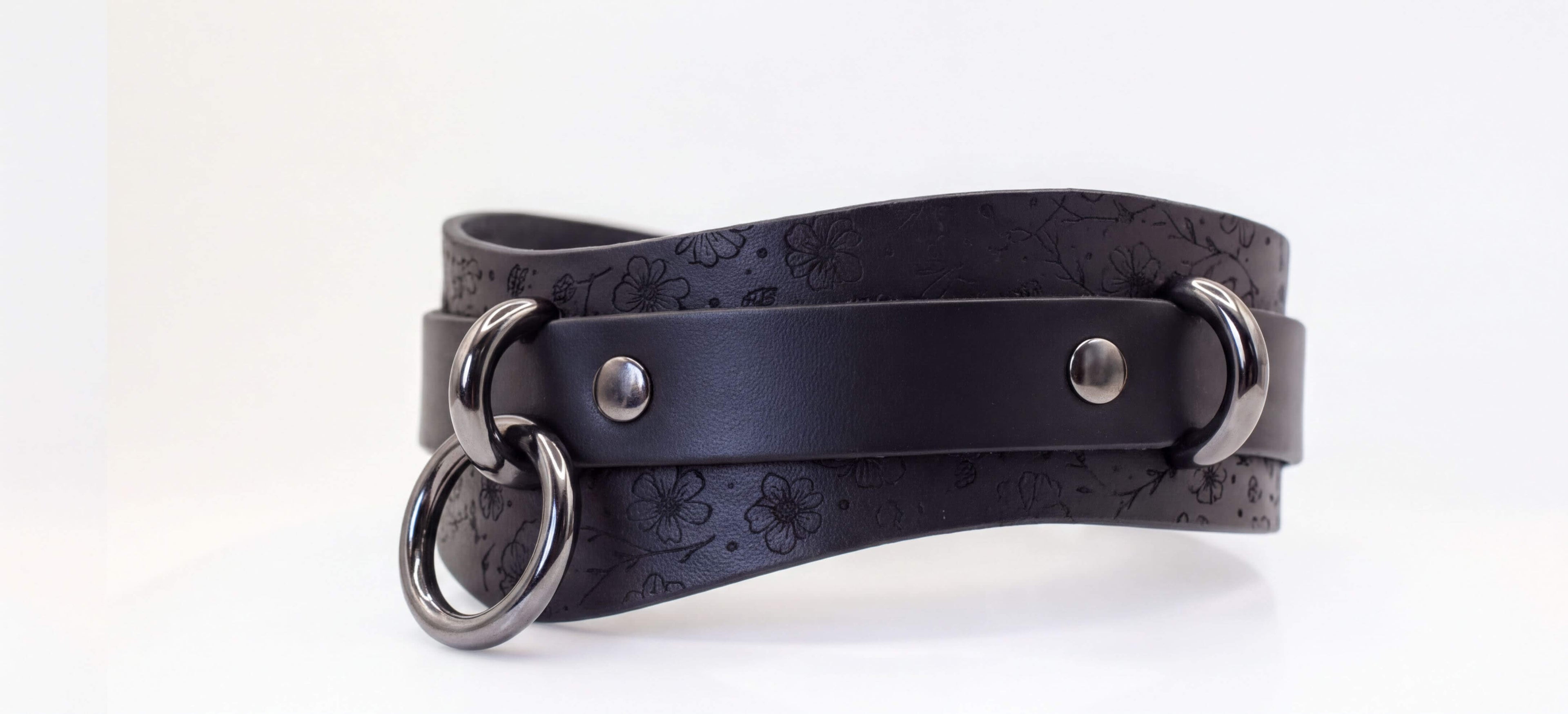 A black leather choker necklace with metal rings and a metal buckle.