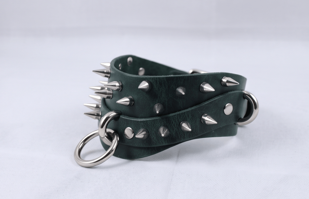 A pair of green leather straps with silver spikes protruding from them, secured with metal rings.