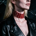 A close-up of a person wearing a black leather jacket with a red spiked choker necklace.