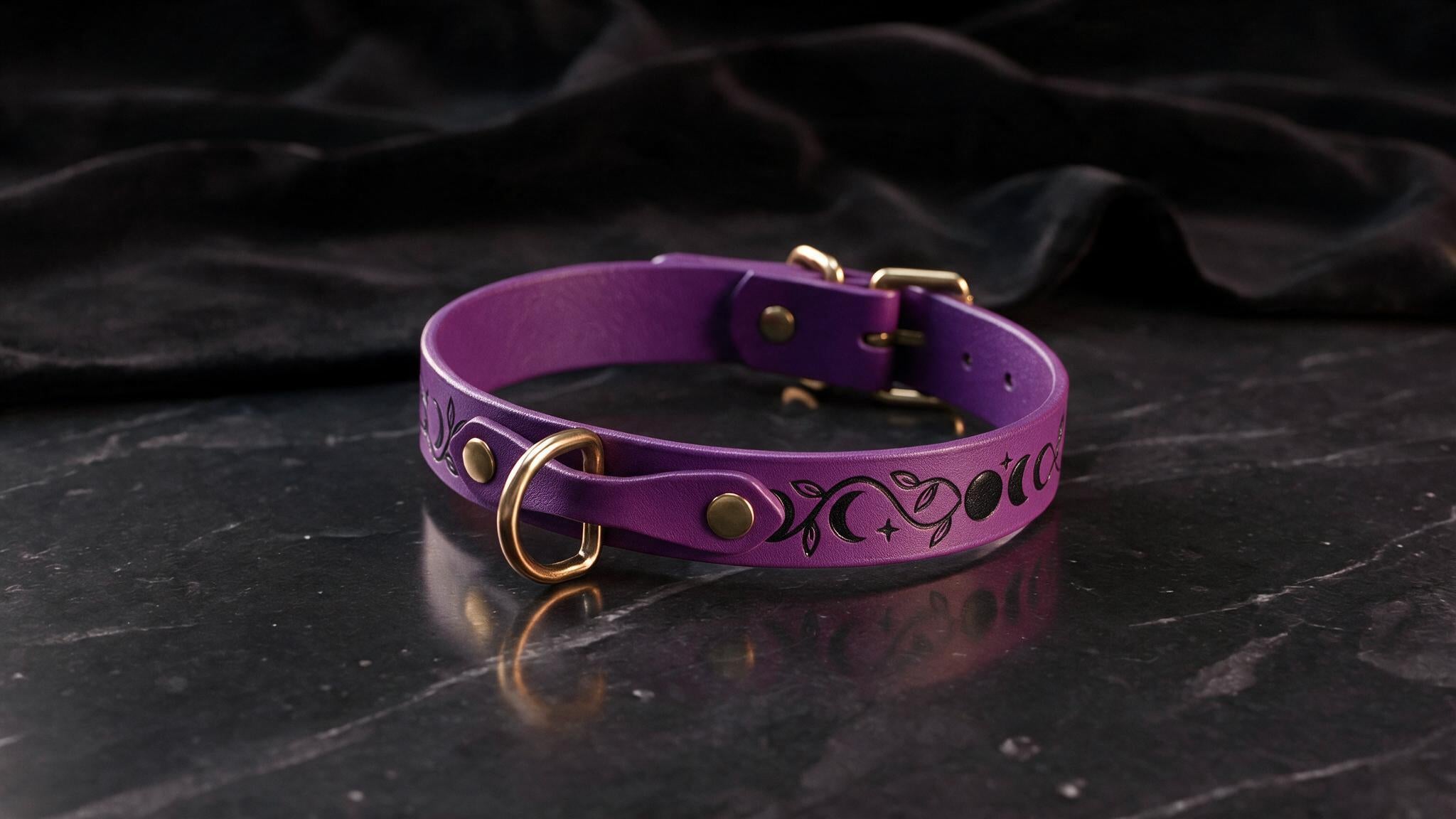 A purple leather collar with a metallic buckle and a design featuring celestial elements, such as stars and planets, is displayed on a dark surface.