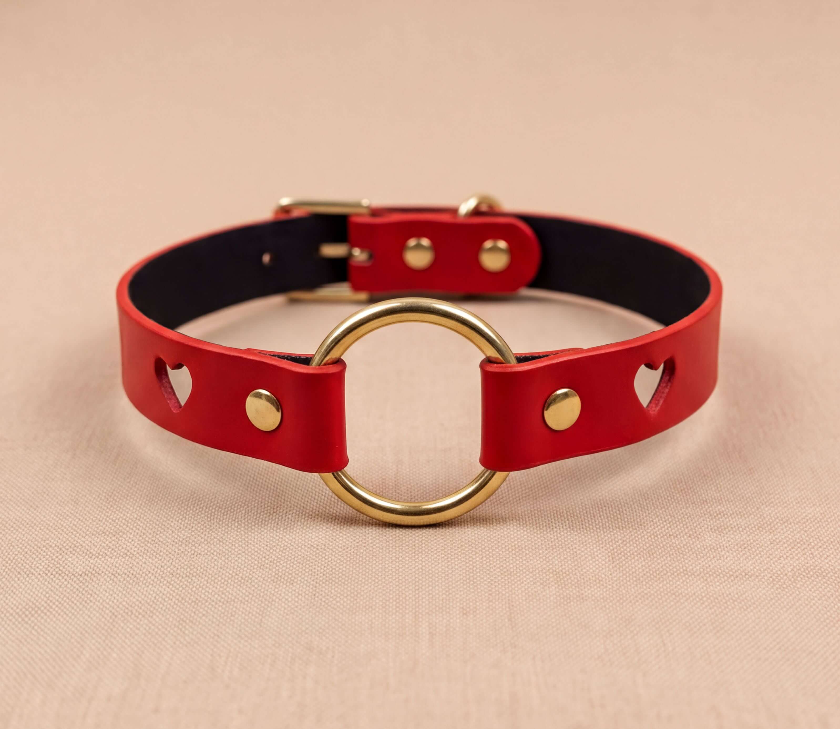 A red leather collar with a gold ring and heart-shaped cutouts on the sides.