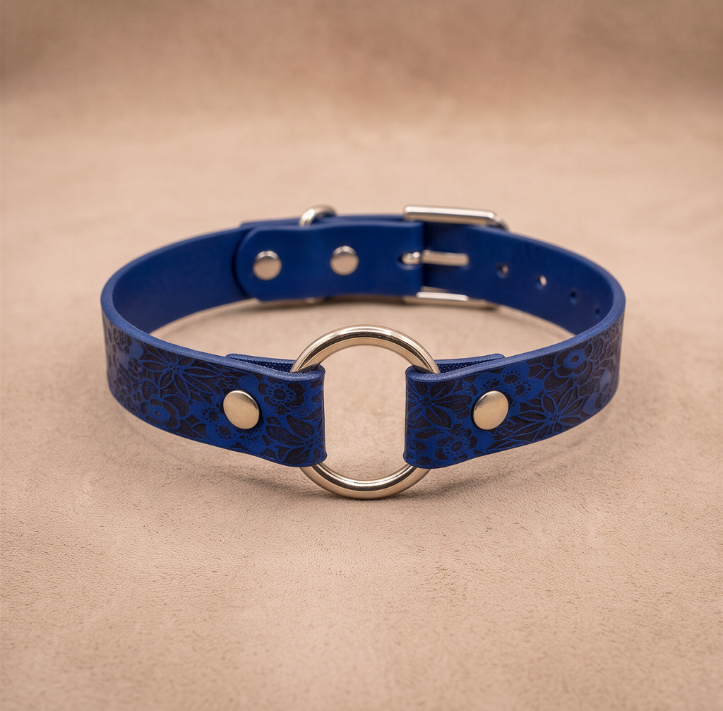 A blue leather collar with a metal ring and buckle, placed on a beige background.