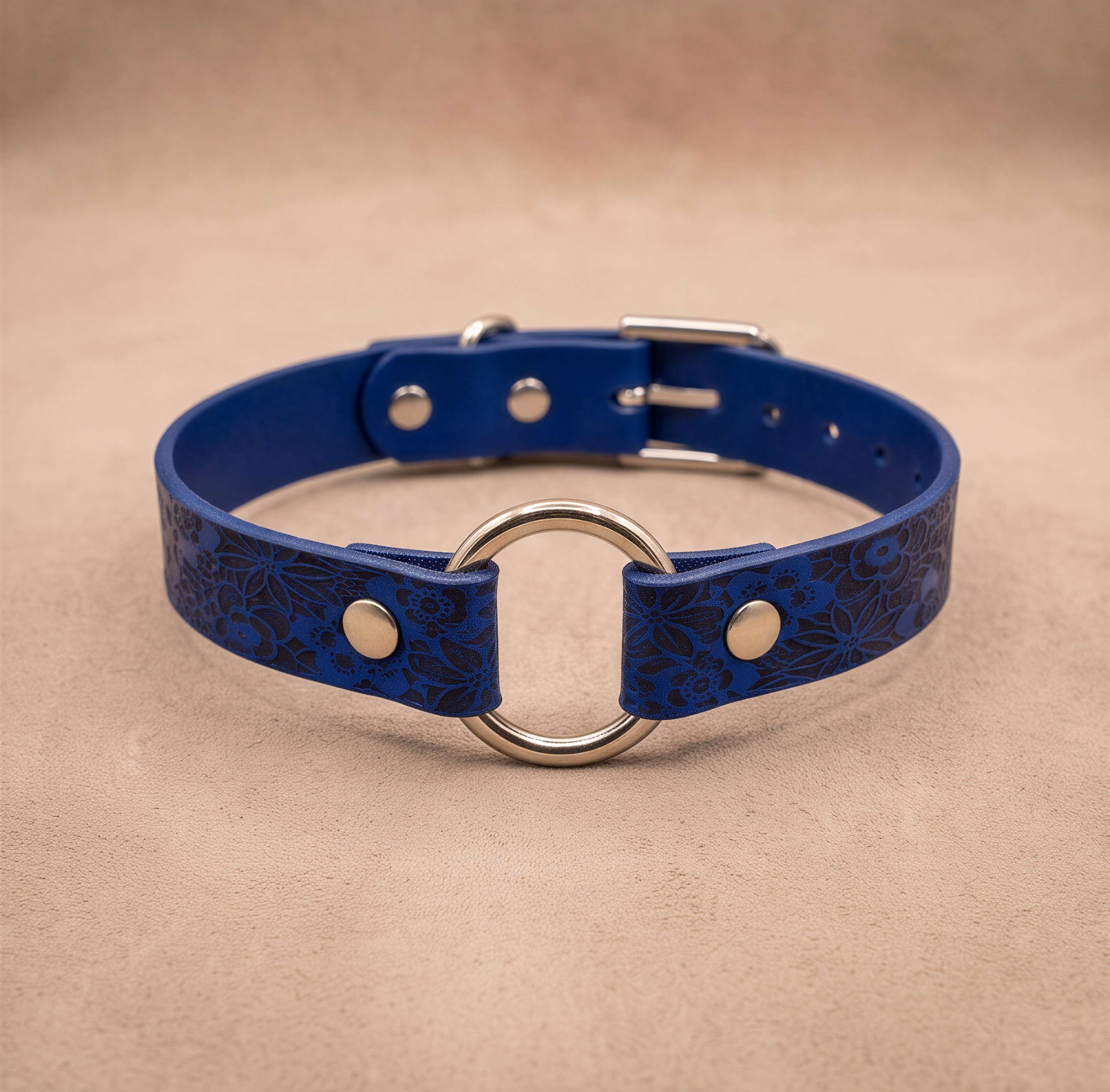 A blue leather collar with a metal ring and buckle, placed on a beige background.