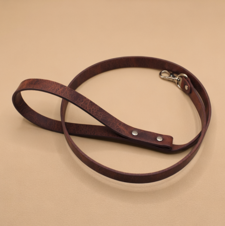 A brown leather dog leash with a metal clasp and buckle is shown on a beige background.