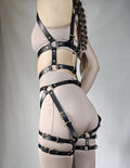 A woman wearing a beige outfit with multiple black leather straps and buckles, posing with her back to the camera.