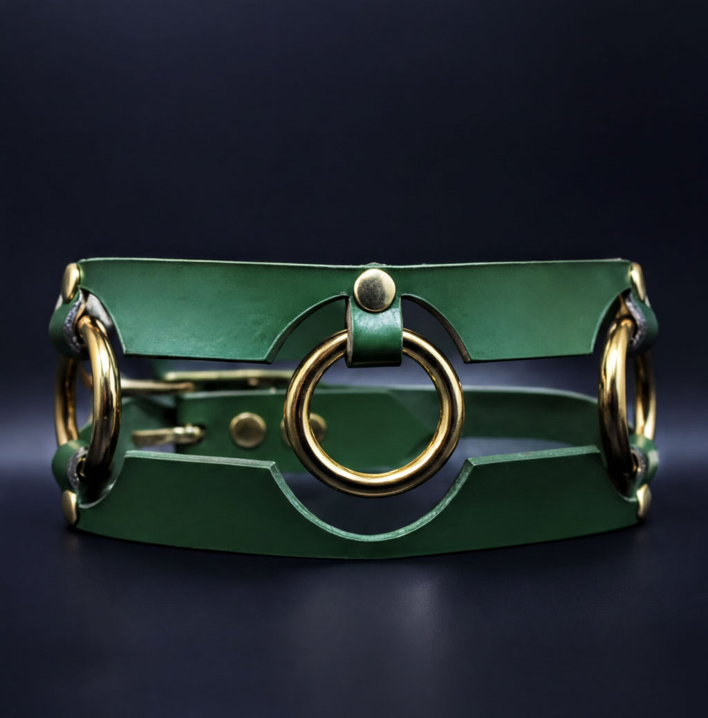 A green leather collar with gold-colored metal rings and a circular cutout in the center.