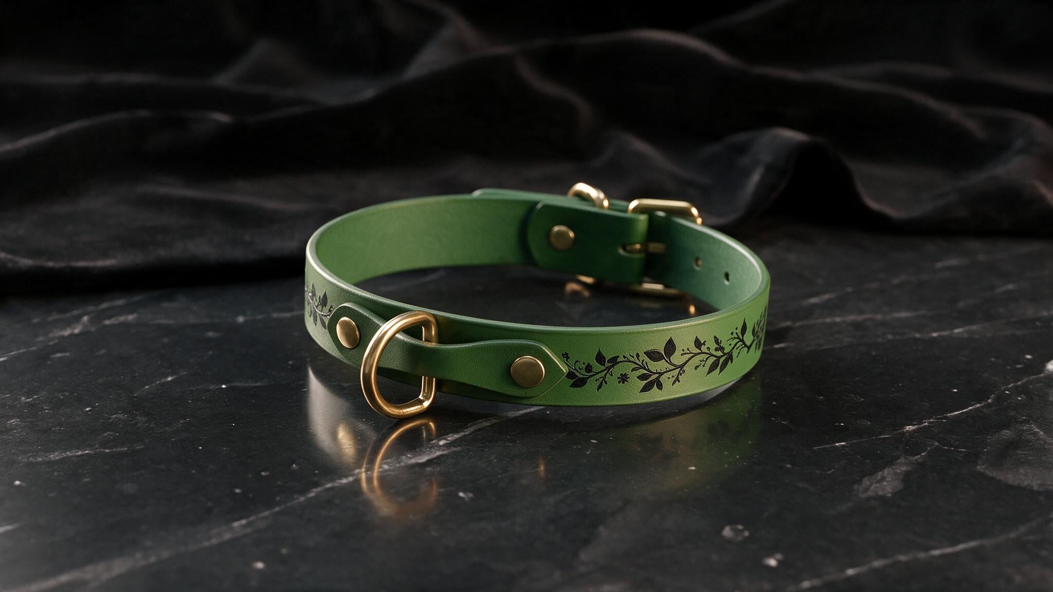 A green leather collar with a floral design and a gold-colored buckle is displayed on a black marble surface.