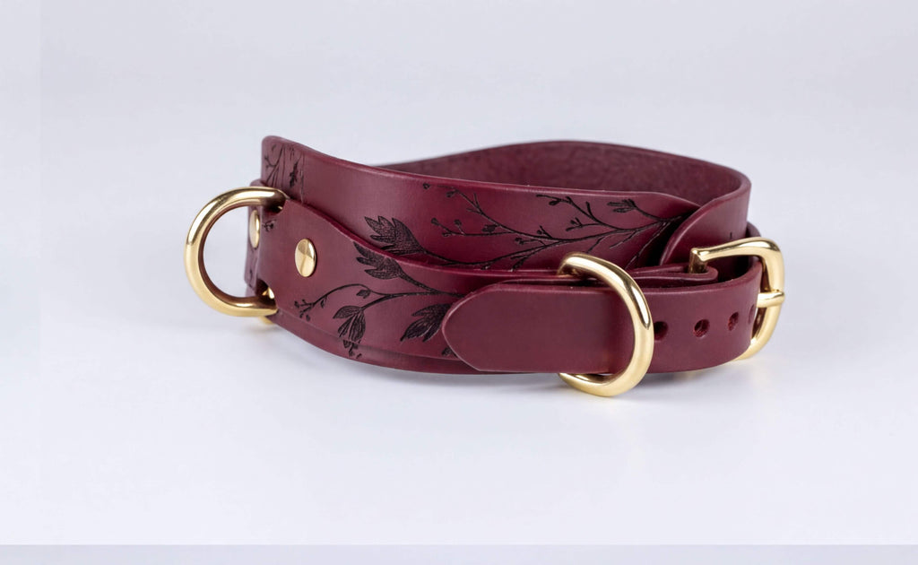 A burgundy leather belt with a floral design and two gold-colored buckles.