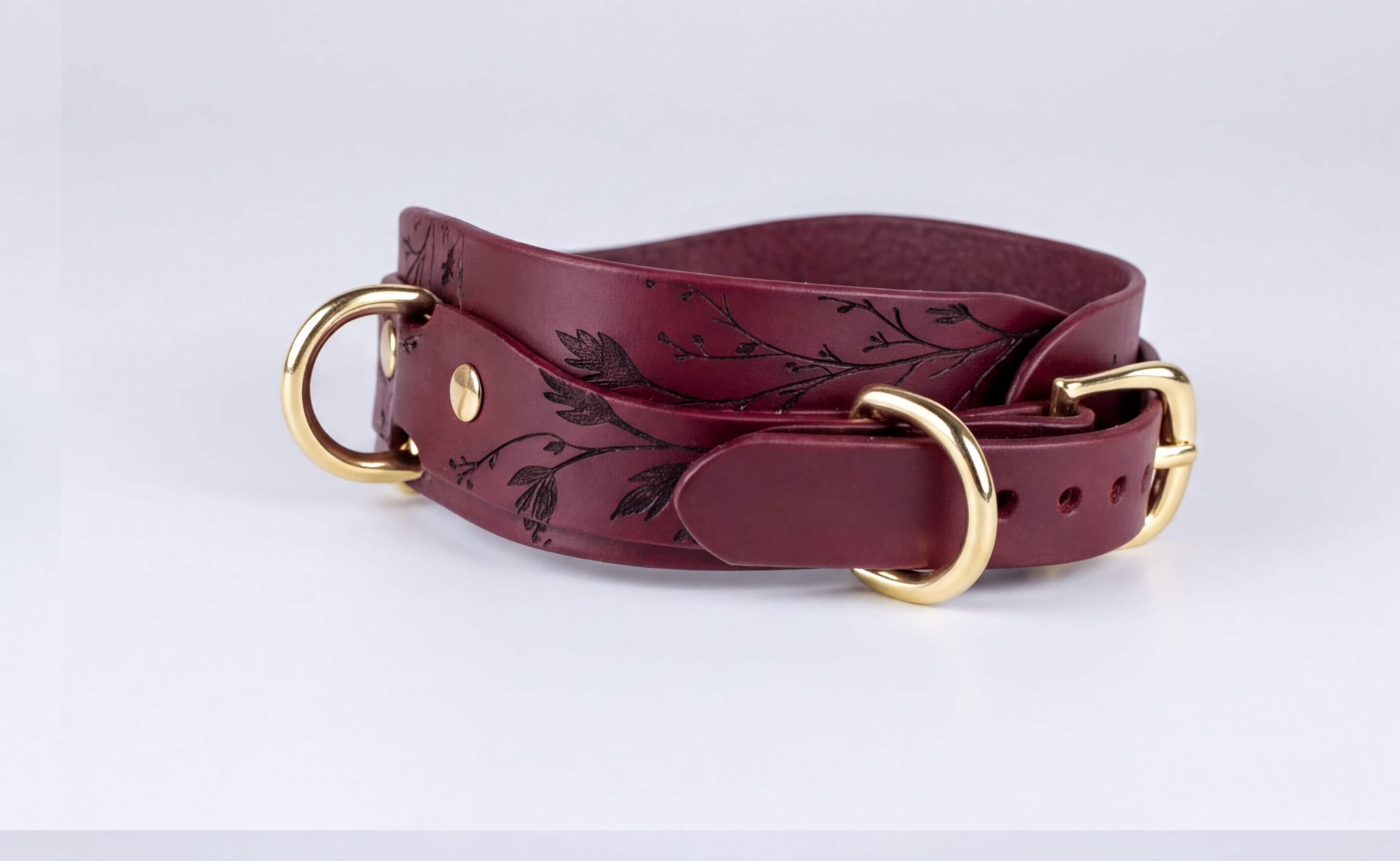 A burgundy leather belt with a floral design and two gold-colored buckles.