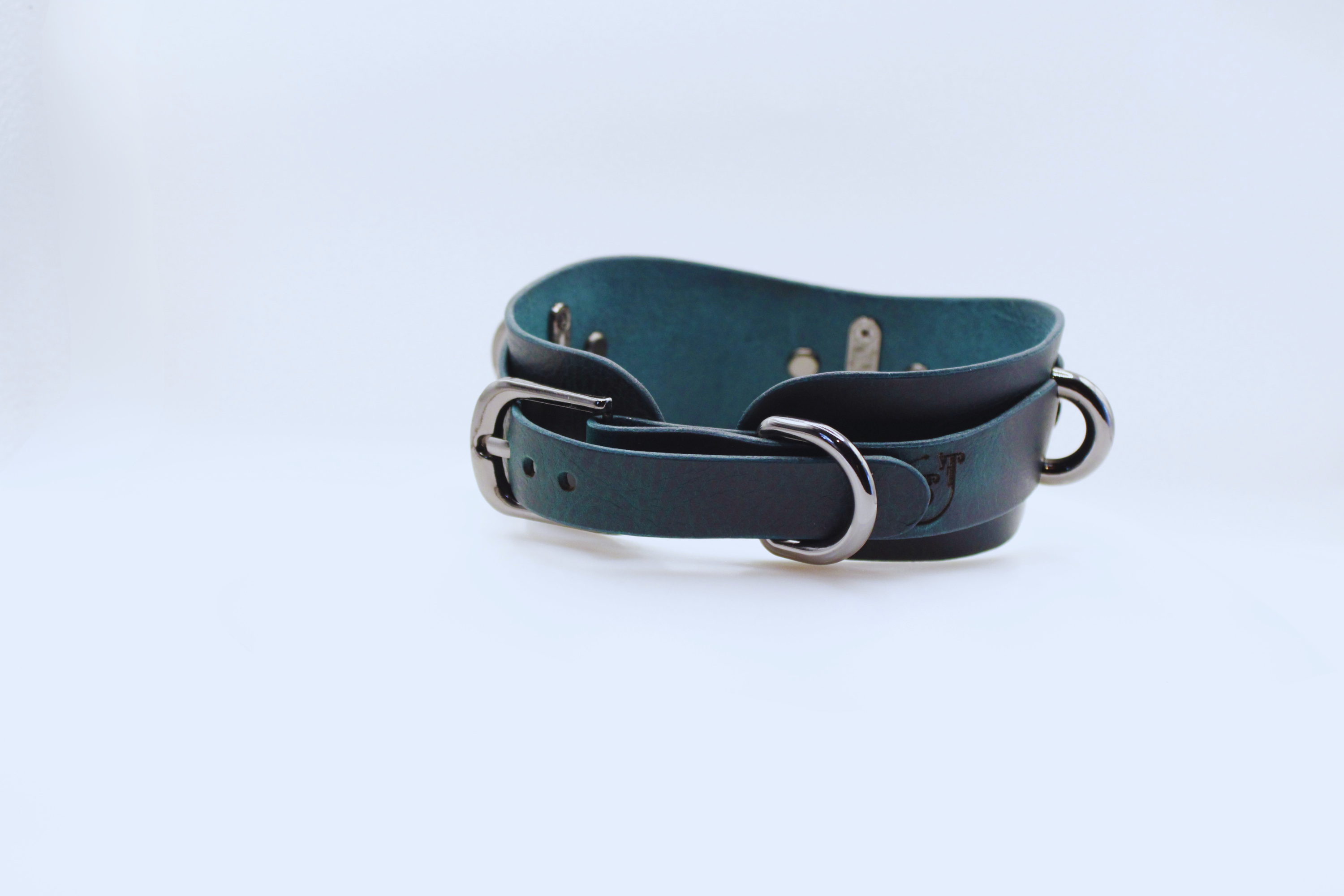 A dark green leather belt with metal buckles and a metal clasp is shown against a white background.