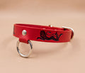 A red leather dog collar with a lion design and metal ring.